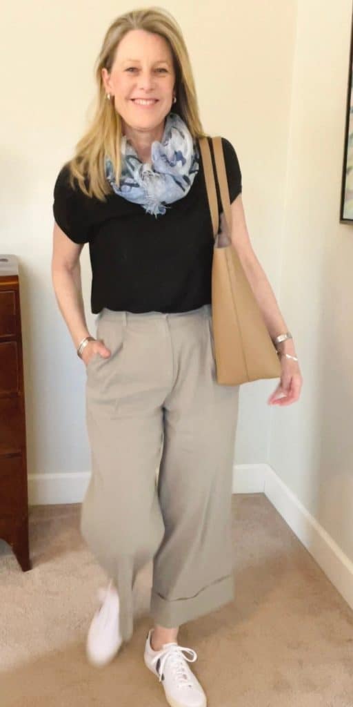 Susan wears pieces from a spring capsule wardrobe - beige trousers and a black tee and blue scarf. She has a Cuyana tote bag over her shoulder.
