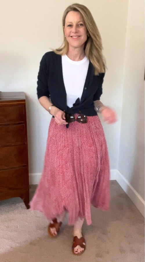 Susan is in a spring travel outfit using the skirt in this capsule - it's paired with a white tee, navy sweater and she is wearing brown slide sandals.
