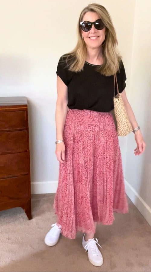 Susan is in a spring travel outfit using the skirt in this capsule - it's paired with a black tee and she is wearing sunglasses and sneakers.