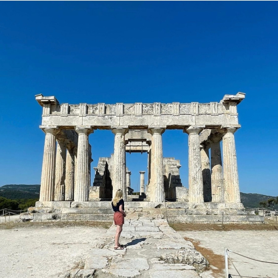 Susan Heinrich stands in front of the Temple of Aphaia, her back to the camera. The temple is located on the island of Aegina in Greece.