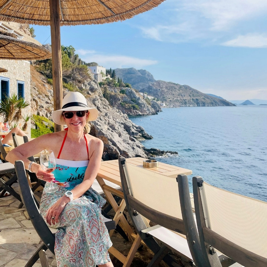 Susan Heinrich sits on a terrace on the Greek island of Hydronetta, with stunning view of the Hydra coast beyond