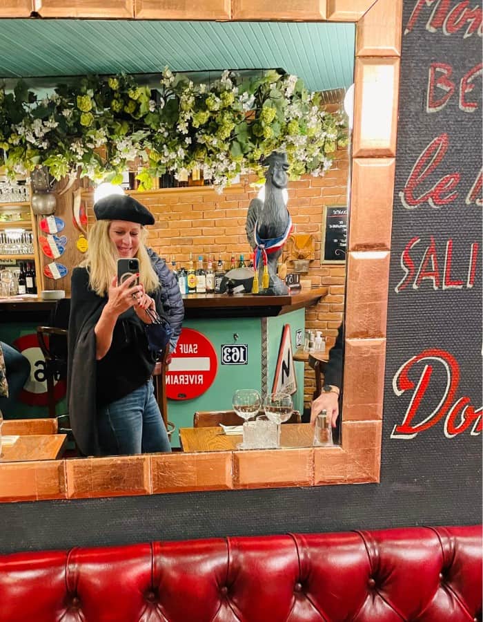 Susan Heinrich stands in front of a mirror, wearing a beret, at one of her favorite Paris restaurants: La Sens Unique. Authentic French food with a quaint atmosphere, near the Avenue des Champs-Élysées.