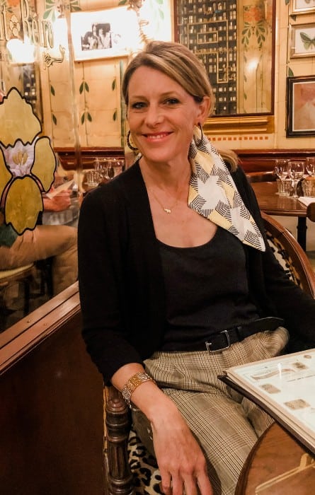 Susan Heinrich sits in a Paris bistro wearing a black top and French tweed trousers