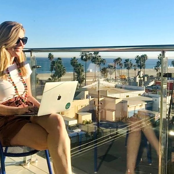 Susan Heinrich sits typing on a laptop and overlooking the Pacific Coast in L.A.