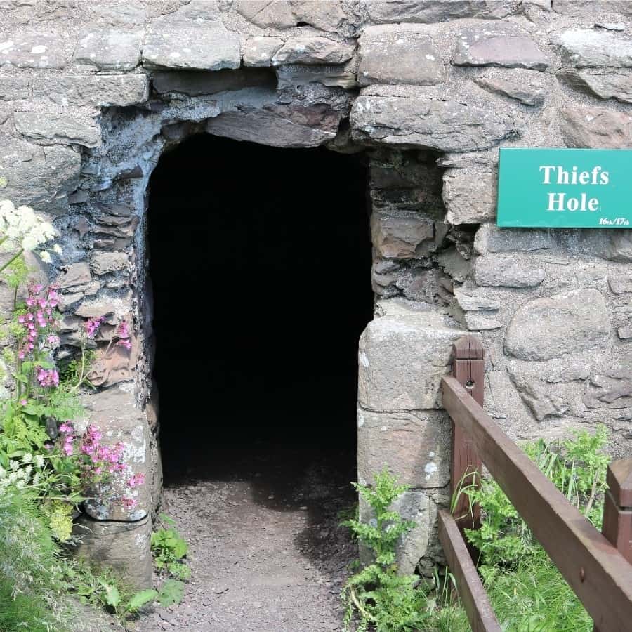 An opening in the stone wall with a sign Thief's Hole at Dunnottar Castle Scotland