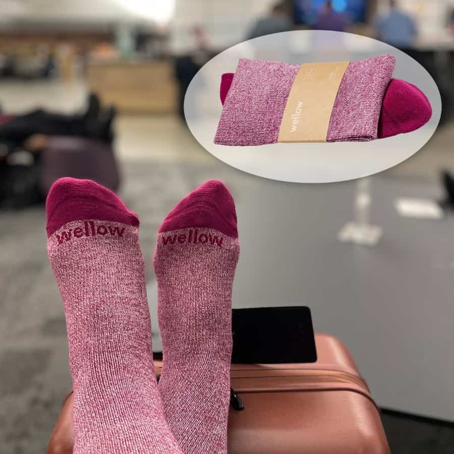 A pair of feet are pictured atop a piece of luggage wearing purple socks with the words Wellow, the brand of the socks.