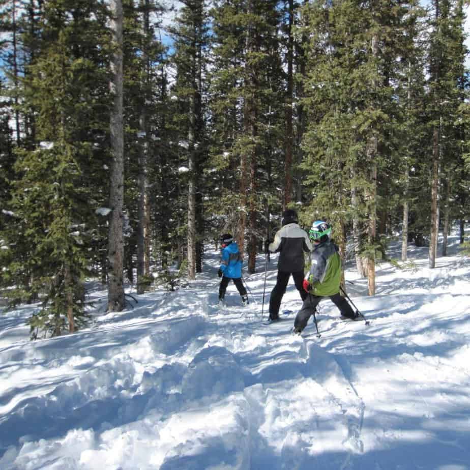 Three children on skis head toward a stand of trees at Winter Park Mountain Colorado
