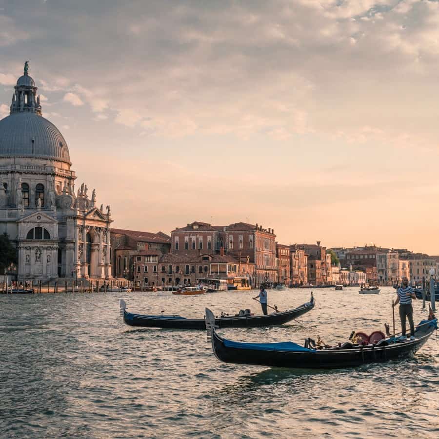 The Grand Canal in Venice at sunset with some gondolas in the foreground.